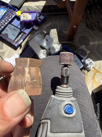 The bronze vase is held next to a Dremel with a cylindrical sanding attachment. Some of the joins have been smoothed